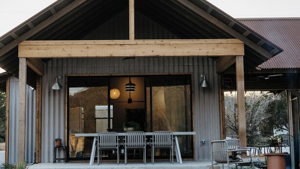 A modern building with a wooden facade, large windows, and a covered patio area with outdoor seating. - Secluded Ranch Stay up to 4 | Near Garner State Park and few steps to Frio River (Concan)