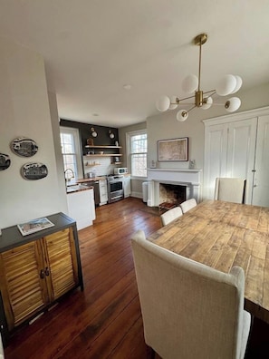 A spacious kitchen with a dining table, white cabinets, and a fireplace.