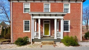 A two-story brick house with a front porch, a yellow door, and a brick driveway. - Historic DT Building, Walk to Shops & Dining (Lynchburg)