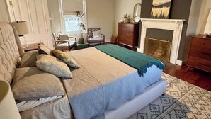 A bedroom with a bed, a ceiling fan, a fireplace, and a patterned rug. - Historic DT Building, Walk to Shops & Dining (Lynchburg)