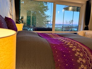 Ein Hotelzimmer mit großem Fenster, einem Bett mit gesteppter Bettdecke und Blick ins Freie.