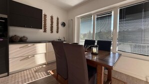 Un coin repas avec une table et des chaises, une cuisine équipée de placards et une fenêtre avec des stores.