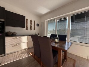 Ein Essbereich mit Tisch und Stühlen, eine Küche mit Schränken und ein Fenster mit Jalousien.