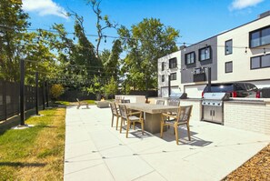 Eine Terrasse im Freien mit Grill, Esstisch und Stühlen.
