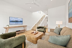 A modern living room with a wooden coffee table, green upholstered chairs, a sofa, a flat-screen TV, a staircase, and a painting on the wall. - Spectrum - Garage - 0.5 mi DT (Bentonville)