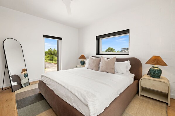 A modern bedroom with a large bed, two bedside tables, a mirror, and a window with a view. - Spectrum - Garage - 0.5 mi DT (Bentonville)
