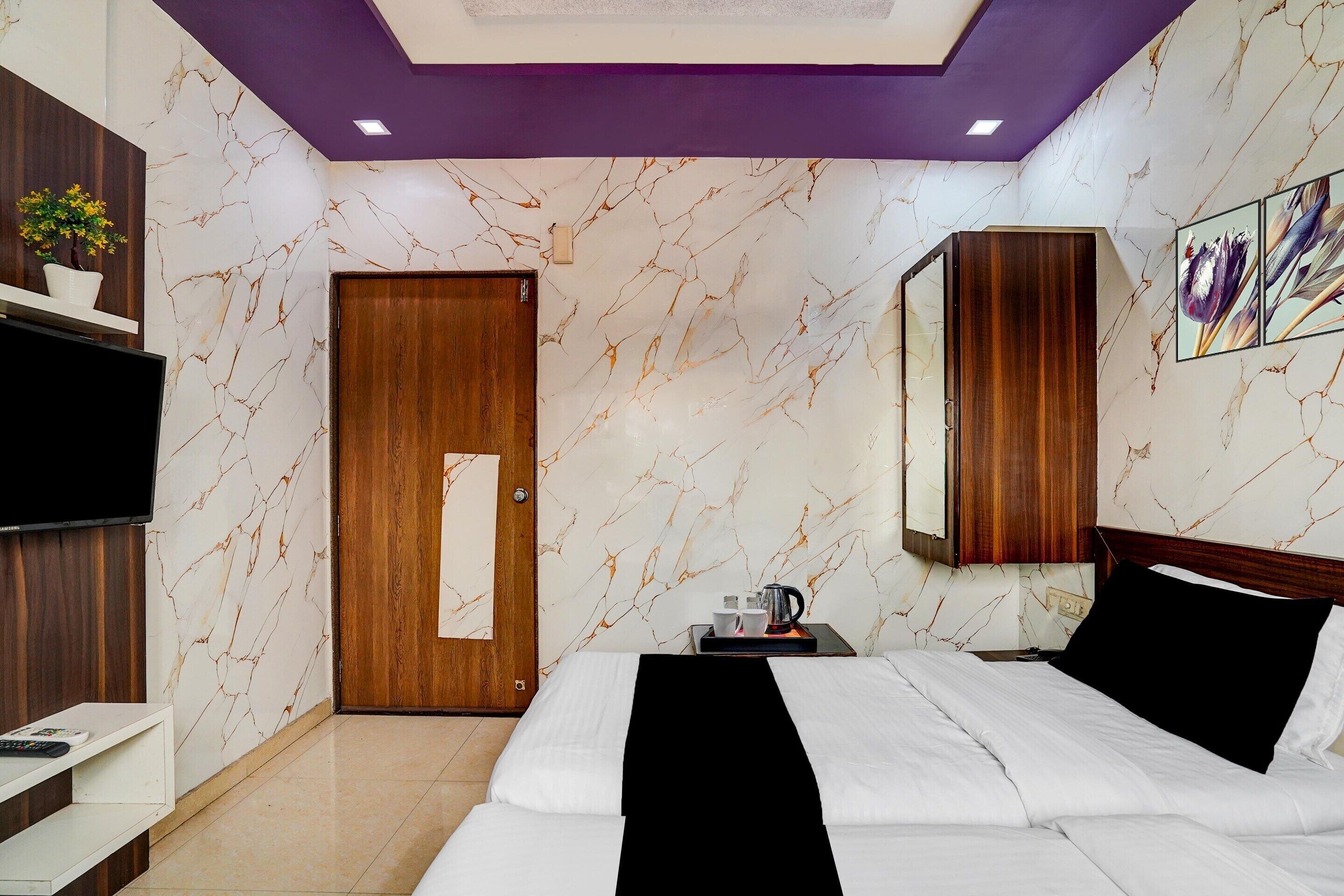 A hotel room with a bed, bedside table, a TV, a wardrobe, and a door.