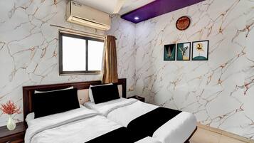 Ein Hotelzimmer mit Bett, Fenster, Deckenventilator, Klimaanlage und Wandbildern.