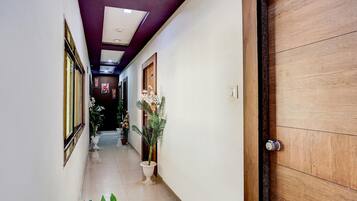 A hallway with a wooden door, potted plants, and a tiled floor.
