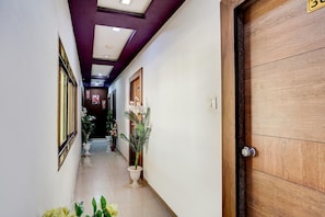 Un pasillo con puerta de madera, plantas en macetas y suelo de baldosas.