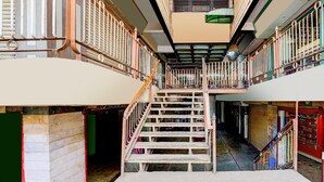 Un interior de varios niveles con una escalera central, barandillas de metal y suelo de baldosas.