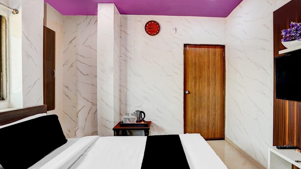 Habitación de hotel con cama, una puerta de madera, una mesita con una tetera, tazas y una bandeja, y un televisor sobre una estantería de madera.
