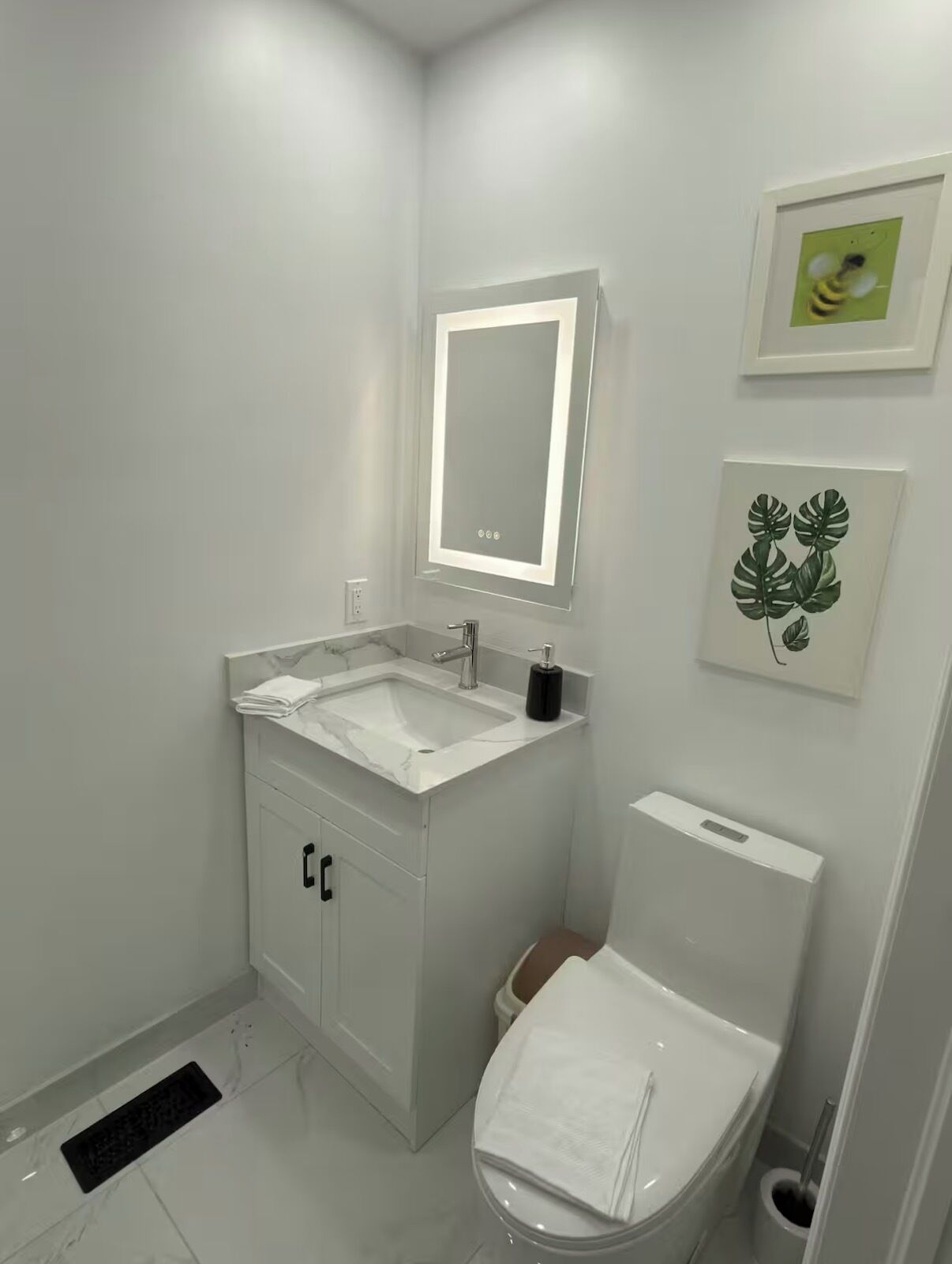 A modern bathroom with a white sink, mirror, toilet, and a small trash bin.