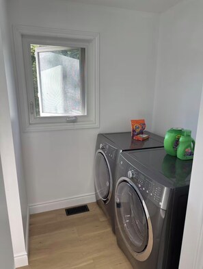 A laundry room with two front-loading washing machines, a window, and a small shelf with detergent bottles.