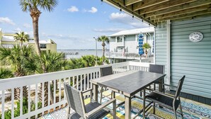 A balcony with a table and chairs, overlooking a beach and a pier.