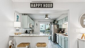 A kitchen with a central island, white cabinets, a ceiling fan, and a 'HAPPY HOUR' sign.