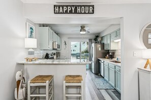 Une cuisine dotée d’un îlot central, de meubles blancs, d’un ventilateur de plafond et d’une pancarte indiquant « HEURE HEUREUSE ».