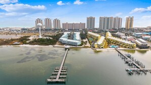 A coastal cityscape with high-rise buildings, a marina, and a long pier extending into the water.