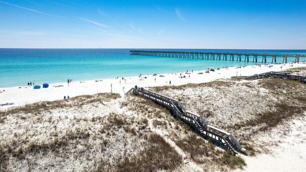 A beach with a wooden boardwalk, sandy dunes, and a pier extending into the water.