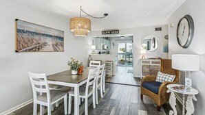 A dining area with a table and chairs, a wicker chair, a hanging light fixture, and a 'HAPPY HOOK' sign.