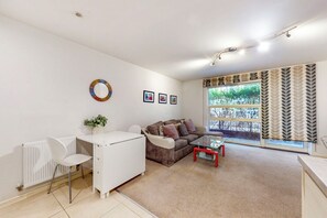 Ein modernes Wohnzimmer mit einer weißen Heizung, einem braunen Sofa, einem Glastisch und einem weißen Schreibtisch mit Stuhl.