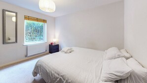 Et soveværelse med en seng, et natbord, et spejl, et vindue med udsigt til træer og en loftlampe.