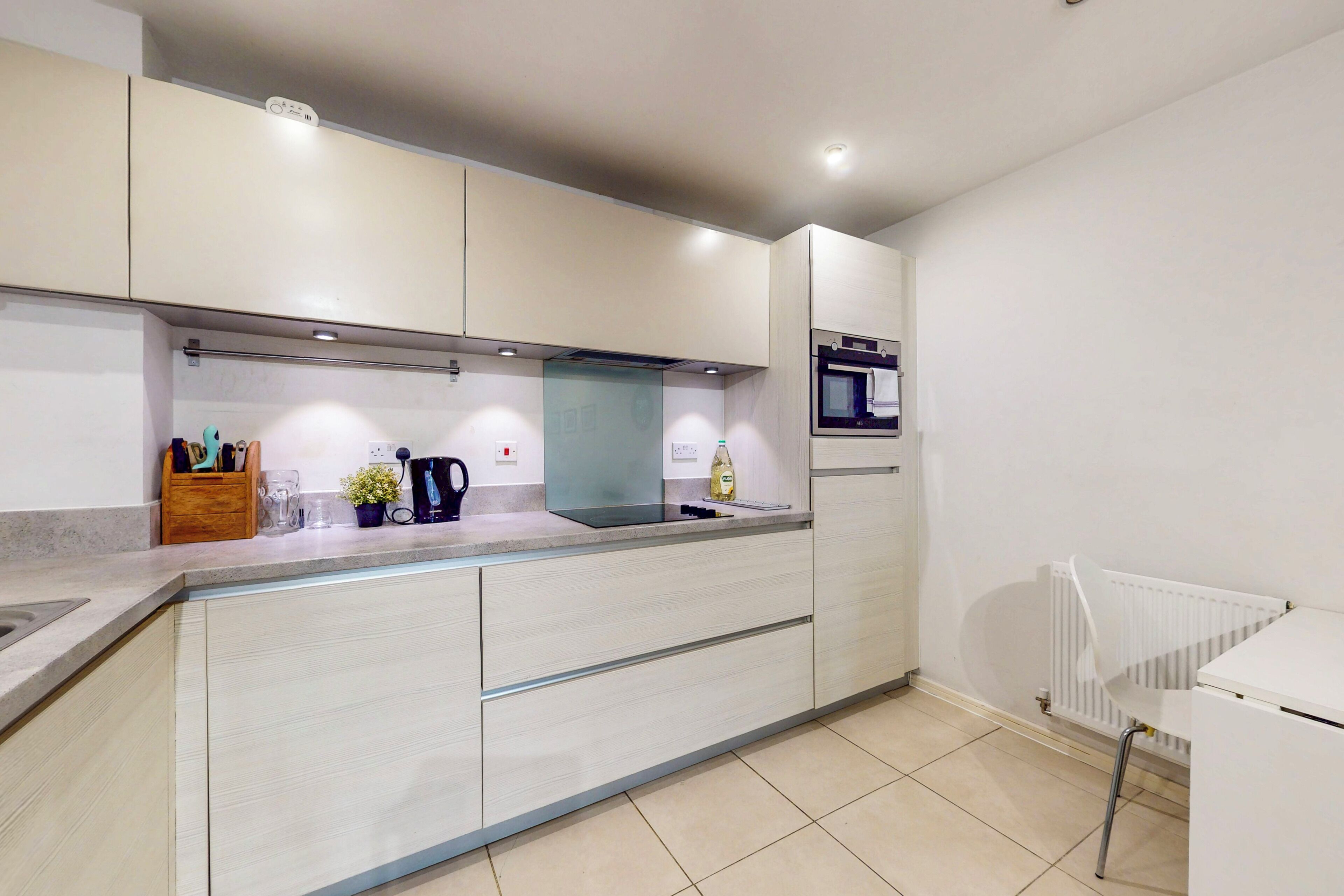 A modern kitchen with white cabinetry, a built-in oven, and a countertop with various appliances and items.