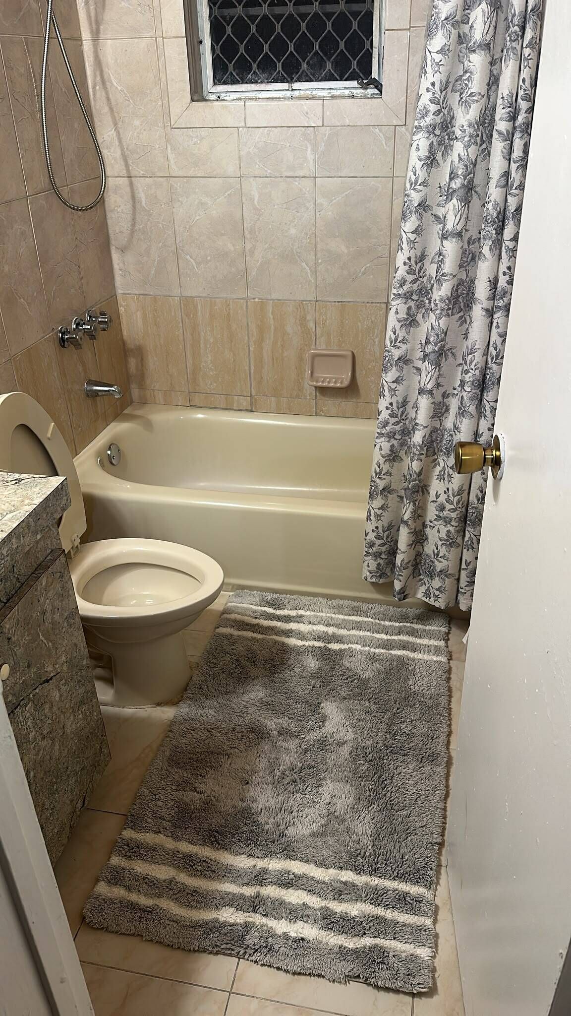 A bathroom with a bathtub, toilet, shower, and a window with a metal screen.
