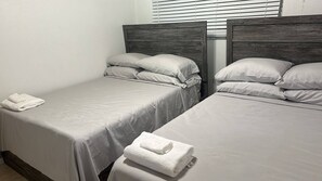 A twin room with two beds, each with a wooden headboard, white bedding, and a folded towel on the floor. - Cozy Nassau Hideaway – Local Island Charm (Nassau)