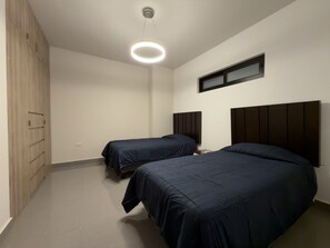 A bedroom with two beds, a ceiling light, a window, and a wardrobe.