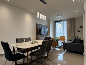 A modern living room with a dining area, a sofa, and a TV mounted on the wall.