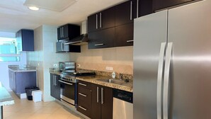 Une cuisine moderne dotée d’appareils électroménagers en acier inoxydable, de meubles de rangement aux couleurs sombres et d’un plan de travail en granit.