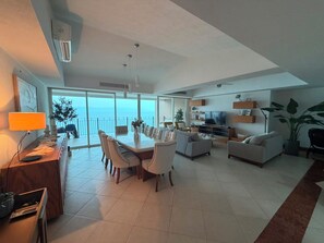 A modern living room with a dining area, a TV, and a balcony with a view. - Luxury 3-Bedroom Apartment with Panoramic Ocean Views at the Grand Venetian (Puerto Vallarta)