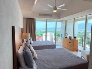 Een moderne hotelkamer met twee bedden, een plafondventilator en een balkon met uitzicht op de stad.