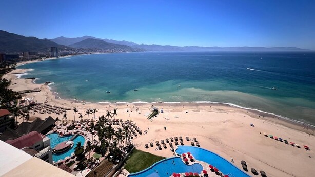 Un complexe hôtelier de bord de mer doté d’une piscine, de chaises longues et offrant une vue sur l’océan et les montagnes.