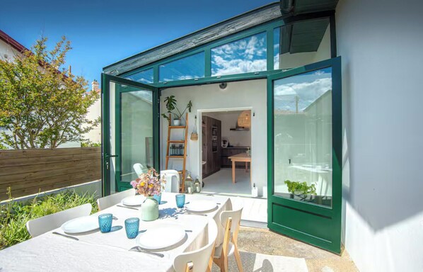 A modern outdoor dining area with a table set for two, a chair, and a vase of flowers.