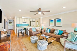 A living room with a sofa, coffee table, ottomans, and a kitchen in the background. - "Oceanfront" Welcome to your ocean view oasis! Steps to beach + Private balcony  (Kapaʻa)