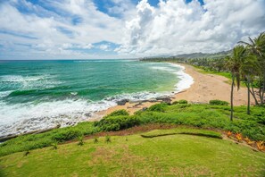 A beach with waves, a clear sky, and greenery. - "Oceanfront" Welcome to your ocean view oasis! Steps to beach + Private balcony  (Kapaʻa)