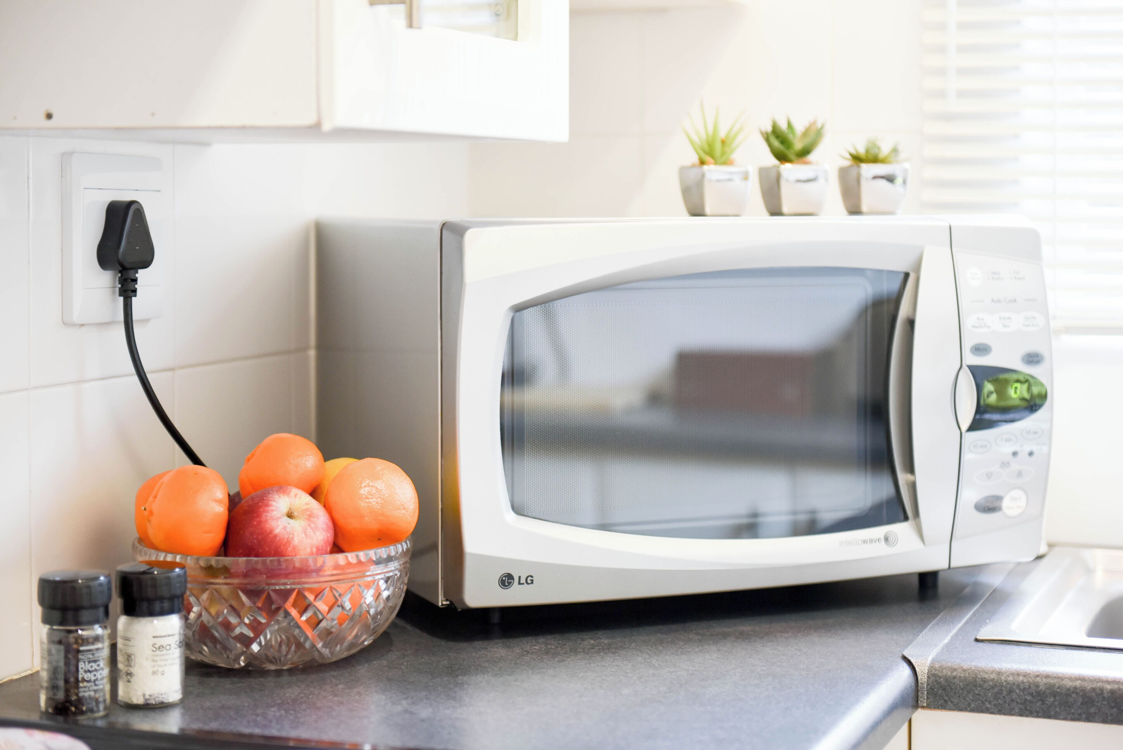 Een keuken met een magnetron, een schaal fruit en een stopcontact.