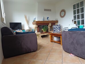 A living room with a fireplace, a television, and two sofas. - Quiet house 600 m from Morgat beach with beautiful wooded garden (Crozon)
