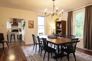 A dining area with a wooden table and chairs, a chandelier, and a view of the kitchen.