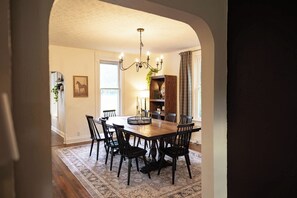 Een eetkamer met een houten tafel, zwarte stoelen, een kroonluchter en een kamerbreed tapijt met dessin.