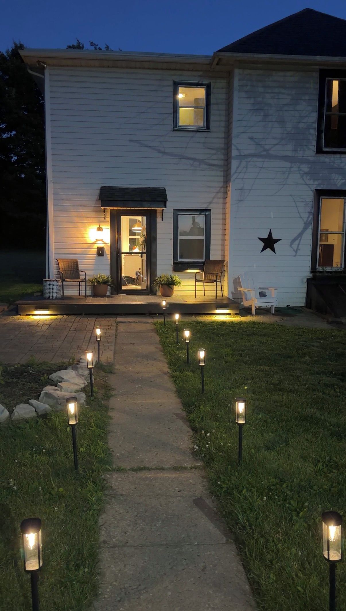 Una casa con porche, mobiliario exterior y un sendero iluminado con luces en el suelo.