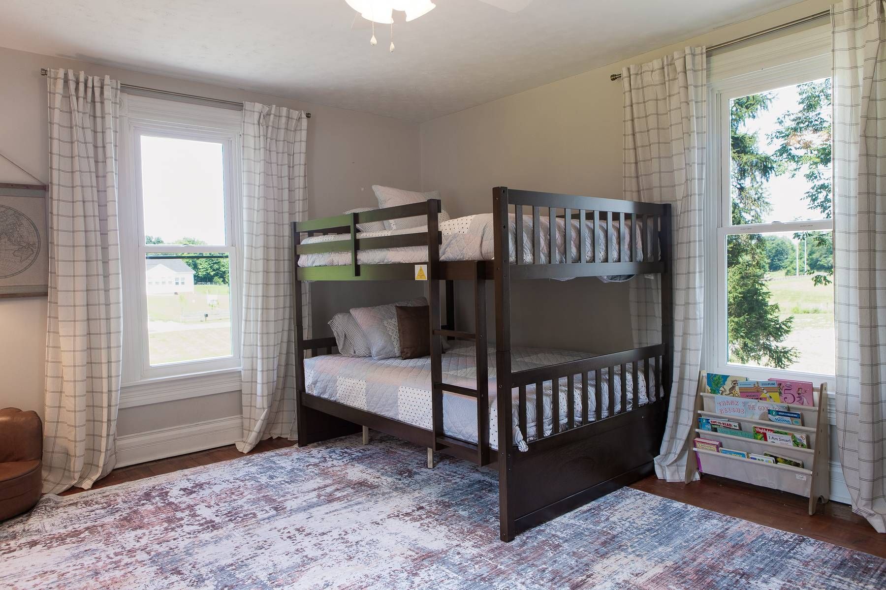 A bunk bed room with a window, a rug, and a bookshelf with children's books.