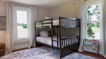 A bunk bed room with a window, a rug, and a bookshelf with children's books.