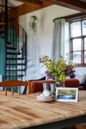 Uma mesa de madeira com um vaso de flores, um jarro de metal, uma tigela de madeira e uma fotografia.