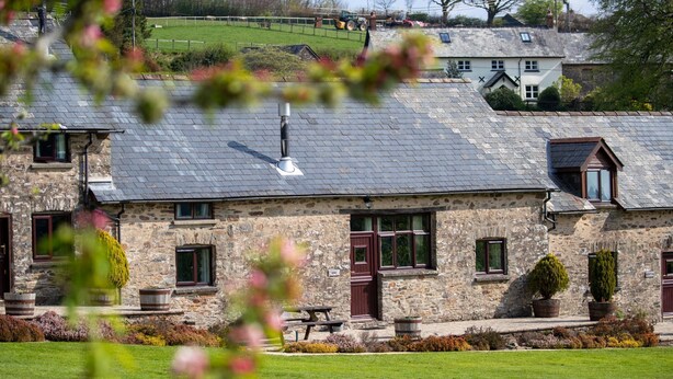 A stone building with a sloped roof, a wooden door, and a window. - Two Exmoor Cottages with Hot Tub | Sleeps 10 (Dulverton)