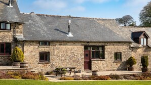 A stone building with a tiled roof, a wooden bench, and potted plants. - Two Exmoor Cottages with Hot Tub | Sleeps 10 (Dulverton)