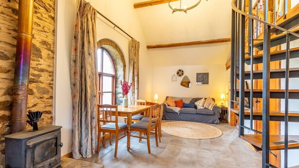 Ein gemütliches Wohnzimmer mit Kamin, Holzmöbeln, einer Treppe und einer Steinwand.