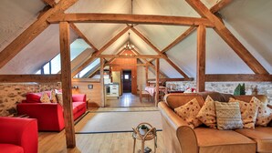 Ein geräumiges Schlafzimmer im Dachgeschoss mit hohen Decken, Holzbalken, einem roten Sofa, einem braunen Sofa und einem Essbereich mit Tisch und Stühlen.